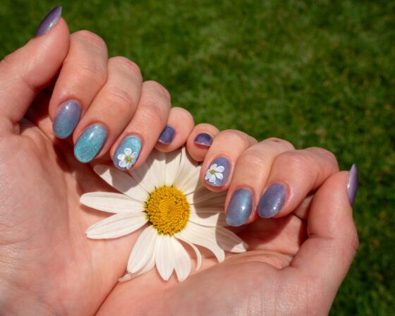 Both hands around a daisy flower, showing the short cat-eye set and the matching floral accents.