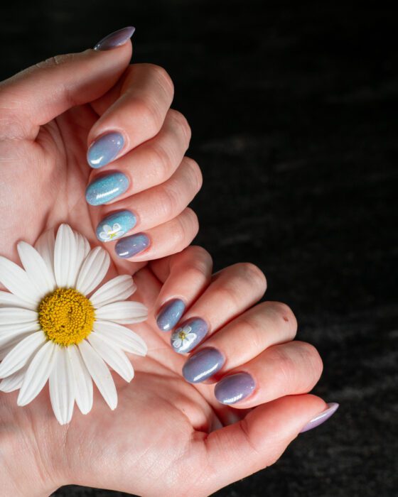 Both hands in direct light, blue-silver cat-eye reflections beside the small white daisy art.