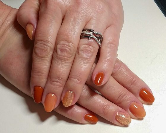 Short oval nails in autumn shades of rust and burnt orange, with two copper glitter accent nails.