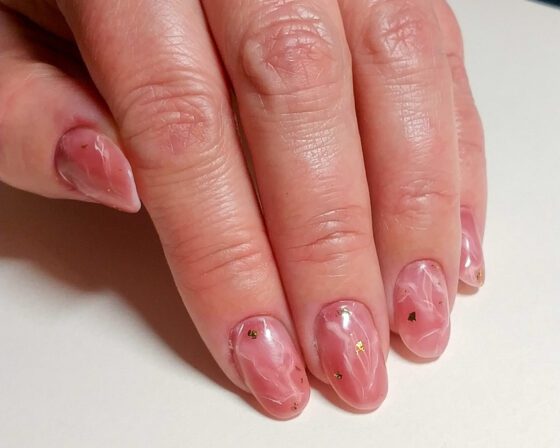 Close view of the same rose quartz marble nails in warmer light, showing the veining and the gold foil.