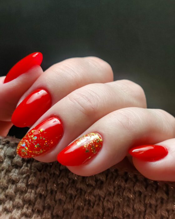 Bright red oval nails with two accent nails fading from gold glitter at the cuticle into red.