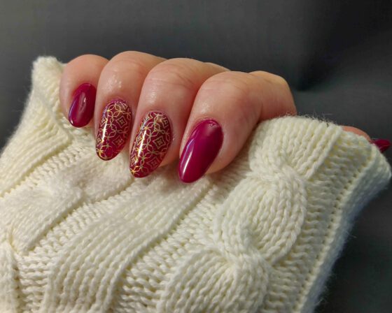 Deep raspberry nails with two accent nails stamped in fine gold lattice and diamond patterns.
