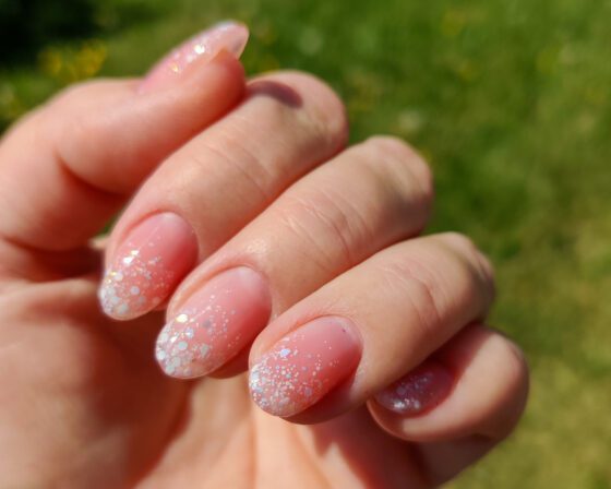 Sheer nude nails in sunlight, with iridescent glitter gathered at the tips.