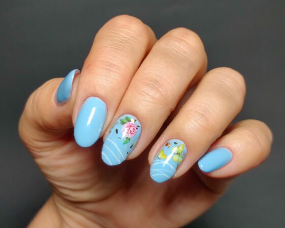 Sky blue oval nails with two accent nails: a pink rose and yellow butterflies with white linework and gold flakes.