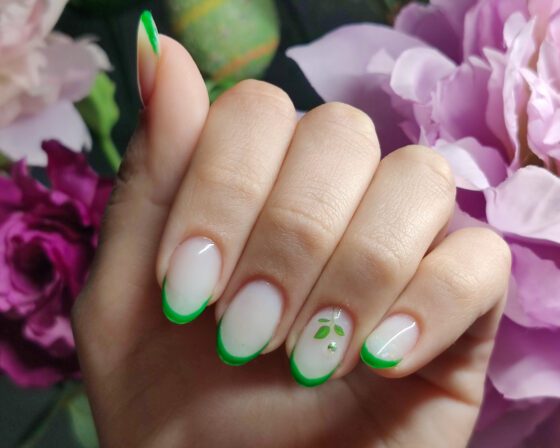 Milky oval nails with fine bright green French tips and one accent nail carrying a green sprig and a crystal.