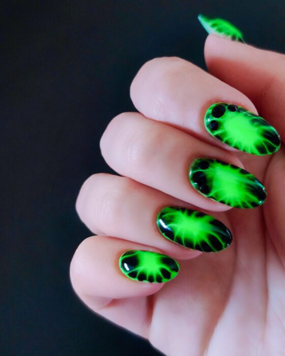 Long oval nails in neon green and black, the green branching outward into fine black filaments, with black stones at the cuticle.