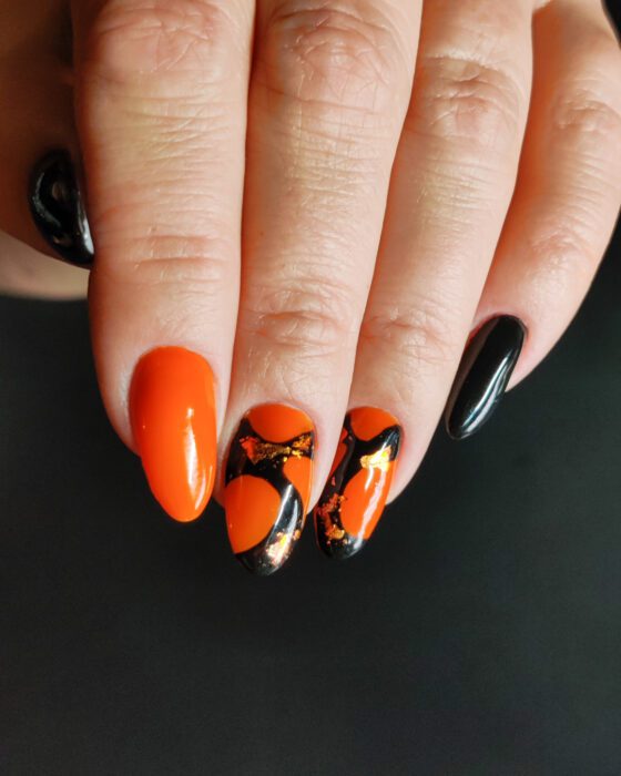 Medium almond nails in bright orange and black, with two accent nails carrying painted arcs and copper foil.