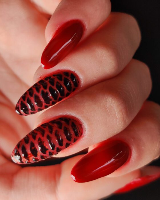 Long almond extensions in deep red, two nails carrying a raised black reptile-scale pattern.