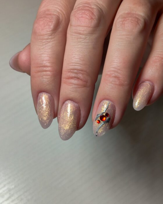 Medium almond nails in champagne shimmer, with one accent nail carrying a silver line and three red stones.