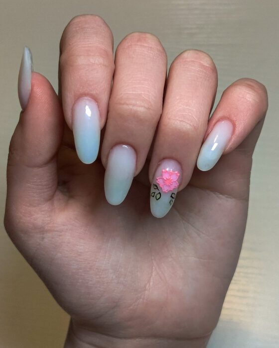 Long milky white almond extensions, one nail carrying a raised pink blossom with painted leaves.