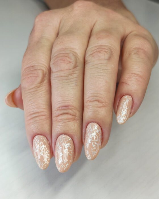 Medium almond nails in warm nude with a white pearl baroque pattern stamped across every nail.