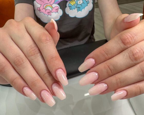 Long coffin extensions in a pink to milky white fade with fine shimmer, both hands held together.