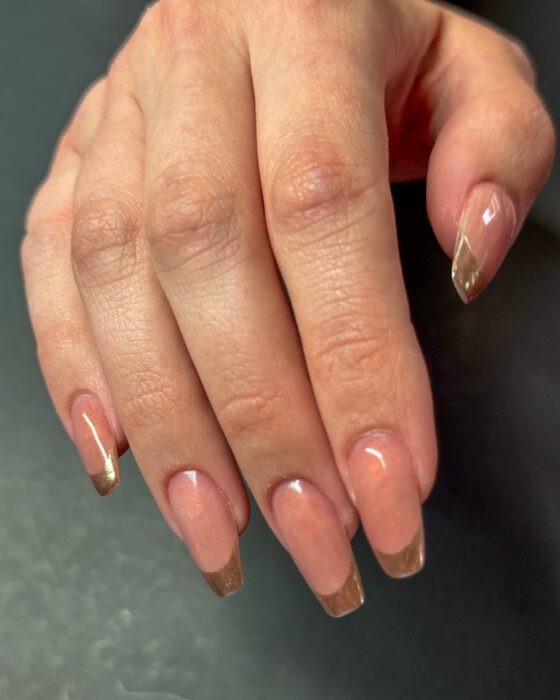 Medium coffin extensions in sheer pearl pink with gold chrome French tips, against a dark background.
