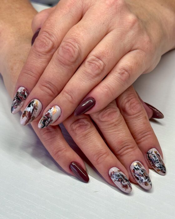 Long almond nails in burgundy and white marble with copper foil, next to flat burgundy nails.