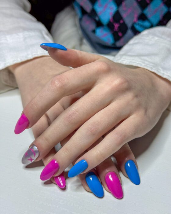 Long almond extensions alternating hot pink and bright blue, with one silver chrome nail carrying hand-painted pink crosses.
