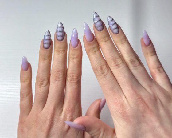 Both hands raised side by side, showing the milky lilac set and the patterned accent nails.