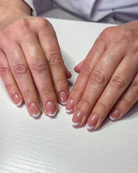 Both hands flat on a white table, the same white tip repeated evenly across all ten nails.