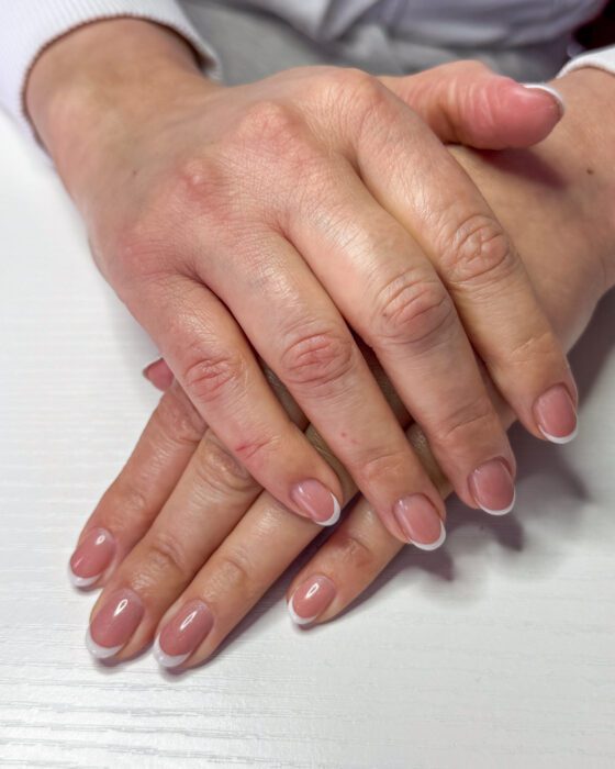 Two hands resting one over the other, short rounded nails in a sheer pink base with narrow white French tips.