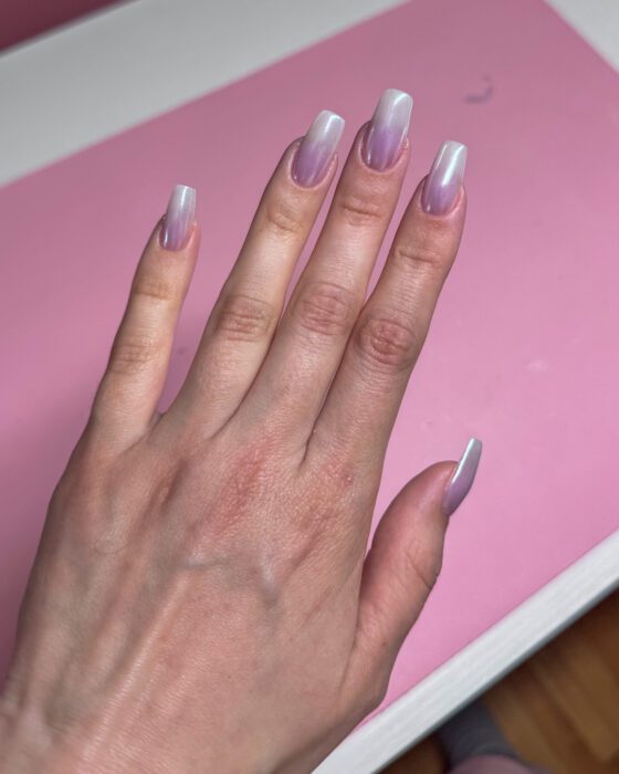 One hand over a pink surface, long coffin nails in a lilac-to-pearl gradient with a chrome finish.