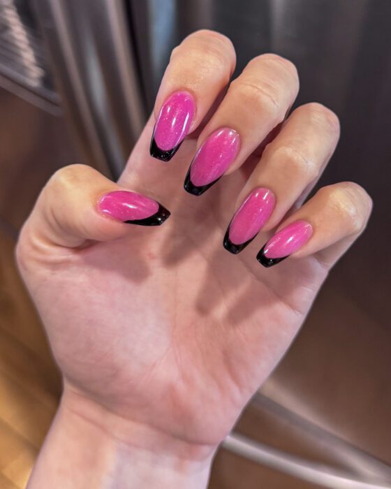 A hand curled toward the camera, long coffin nails in bright shimmering pink with wide black French tips.