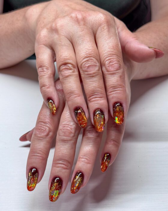 Crossed hands showing the full burgundy-to-amber palette and reflective foil on every nail.