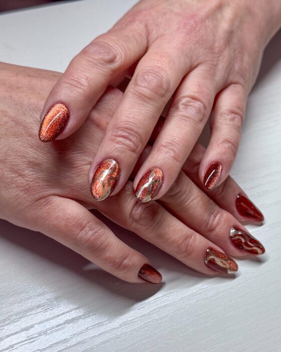 Medium almond nails in a copper and burgundy cat-eye, several of them carrying curved gold line accents.