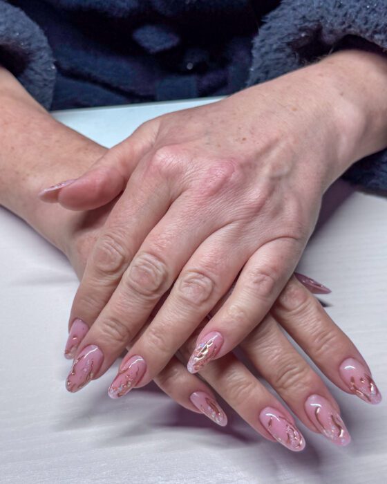 Long oval nude-pink extensions with irregular gold chrome details and fine glitter toward the tips.