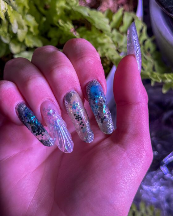 Reflective flakes and glitter catching the light across the extra-long nails.