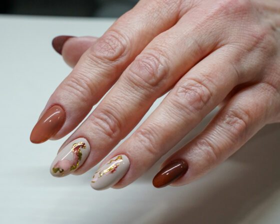 Medium oval nails in warm tan and caramel browns, with two cream accent nails carrying rose-brown and gold slider motifs.