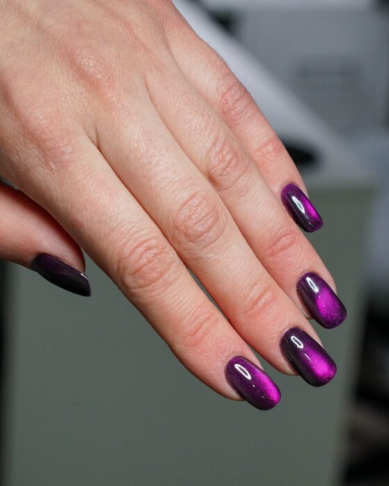 The purple hand at a side angle, the reflection shifting across the nails.
