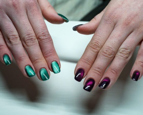 Both hands together, green cat-eye nails on one hand and purple on the other.