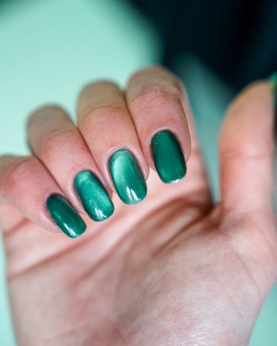 The green hand curled inward, teal cat-eye reflection along the nails.
