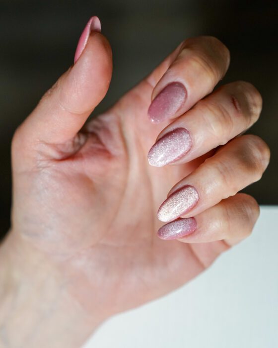 One hand curled inward, pink cat-eye reflection across medium oval nails.