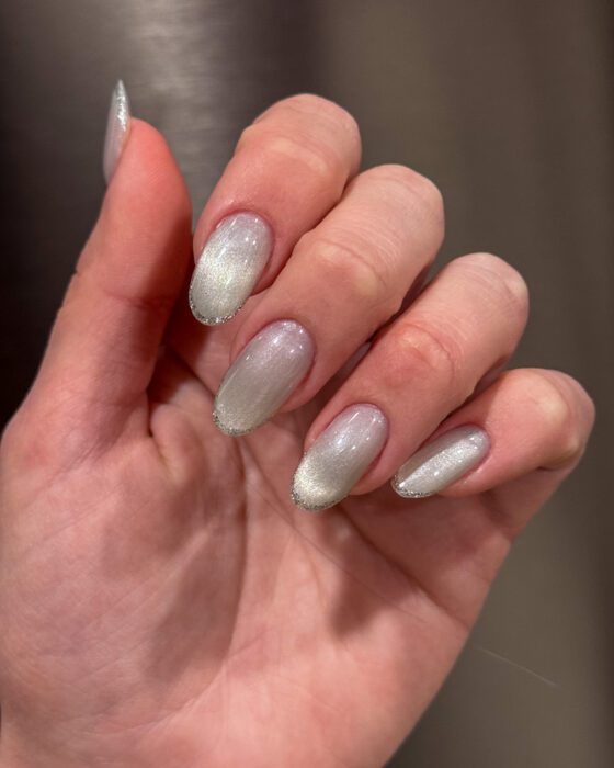 Close view of medium oval nails in a pale silver cat-eye finish with a thin silver glitter French edge.