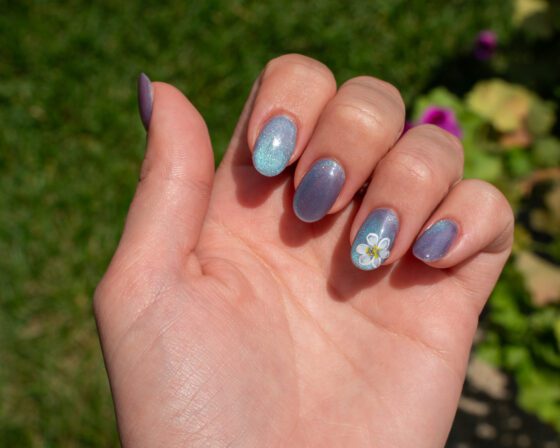 One hand outdoors, lilac and blue cat-eye reflection with a single white daisy accent nail.