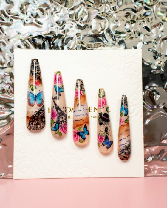 Five detached nude nail-art sample tips with colourful butterflies, roses, black ornamental detail, script and fashion-style graphic motifs.