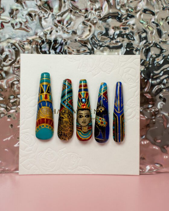 Five detached Egyptian-inspired nail-art sample tips in turquoise, blue, gold and red with portrait and geometric motifs.