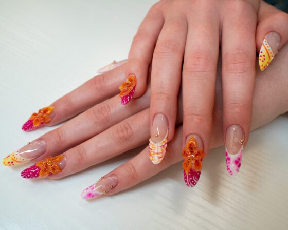 Side view of the extra-long almond nails, with a striped orange and white tip and watercolour pink blooms.