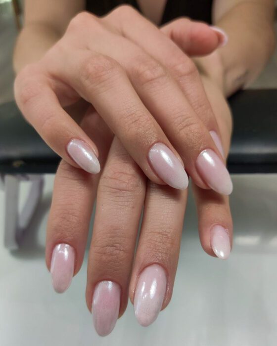 A hand with medium almond nails in a milky pearl-pink chrome finish.