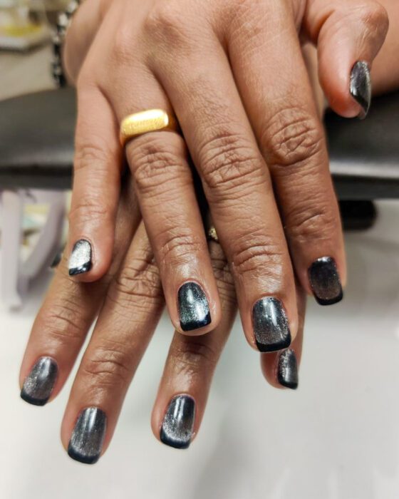 Short dark cat-eye nails with silver-grey reflective bands and a glossy black edge.