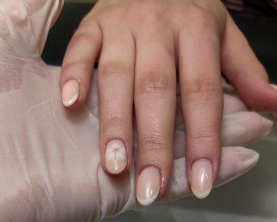 Nude soft-almond nails with thin white French tips and a delicate pink-red floral accent.