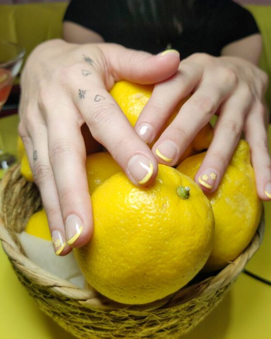 Short oval nude nails with pale lemon French tips and a tiny painted floral accent.
