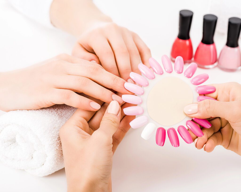 Two hands resting on a white towel beside a fan of pink and nude nail-tip samples, with three bottles of polish behind them
