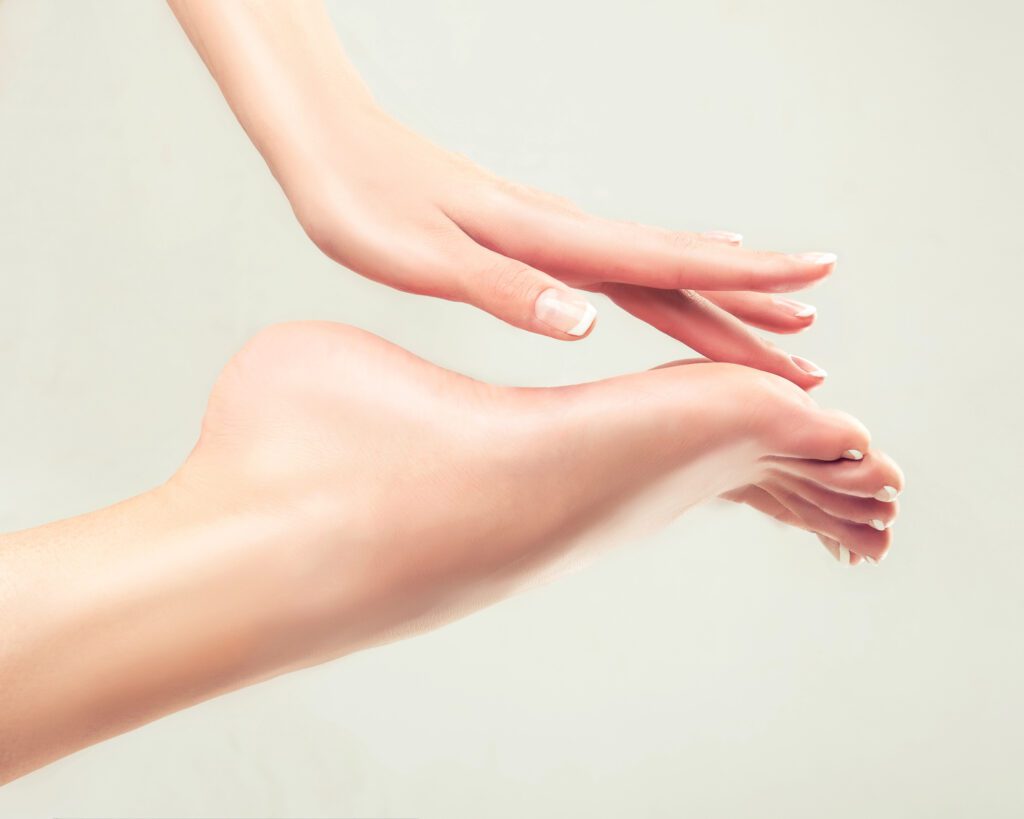 A hand with a French manicure resting against a bare smooth foot with French-tipped toes