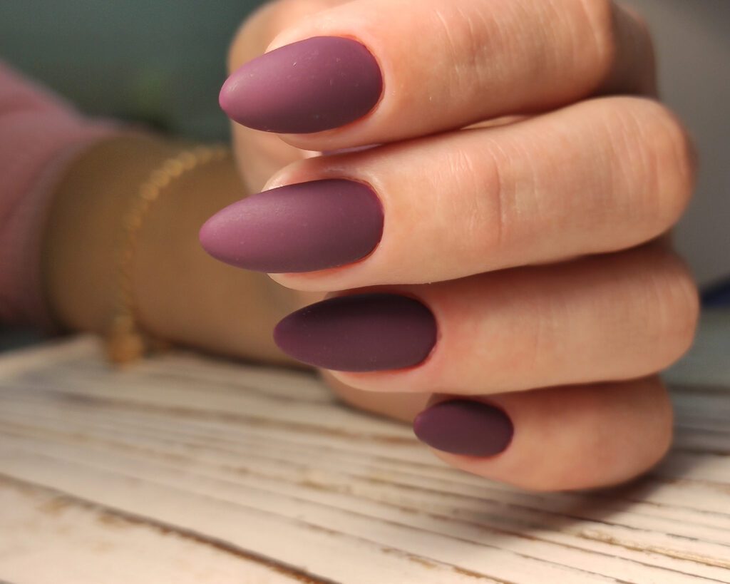 A hand resting on pale wood with almond nails in matte plum and mauve