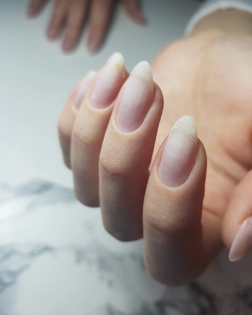 Long almond nails with a clean bare finish and tidy cuticles over a marble surface