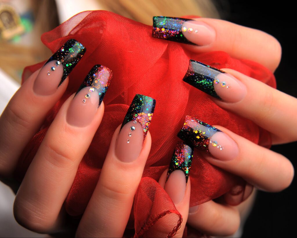 Long extended nails in black and nude with glitter and crystal detail, holding red tulle