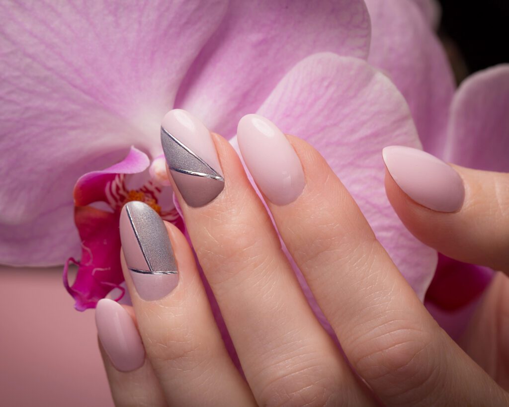 A hand with nails in pale pink and silver geometric detail, held against a pink orchid