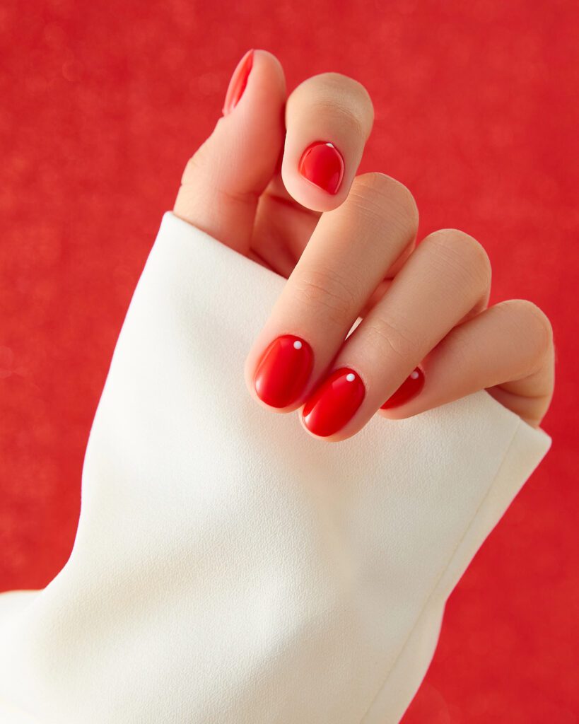 A hand with glossy red nails holding a cream cloth against a red background
