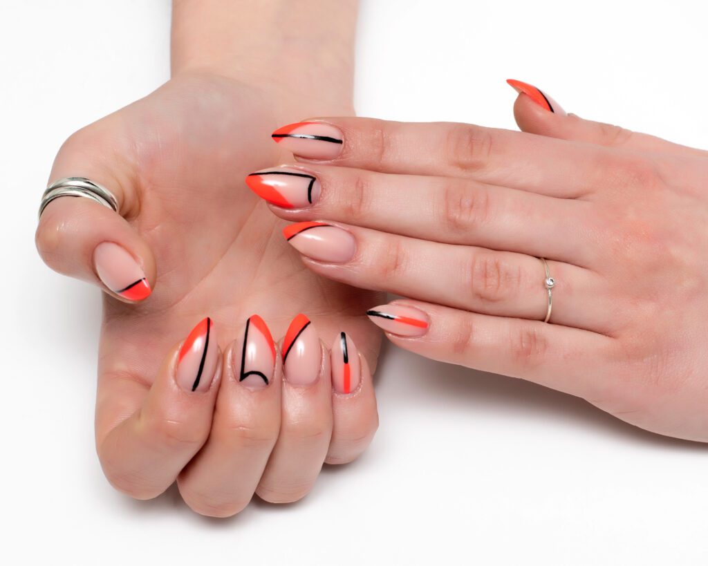 Two hands with nude nails decorated in orange and black abstract line art, wearing plain rings